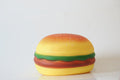 A novelty squishy toy shaped like a hamburger, featuring a yellow textured bun, green lettuce, and red beef patty, set against a plain white background.