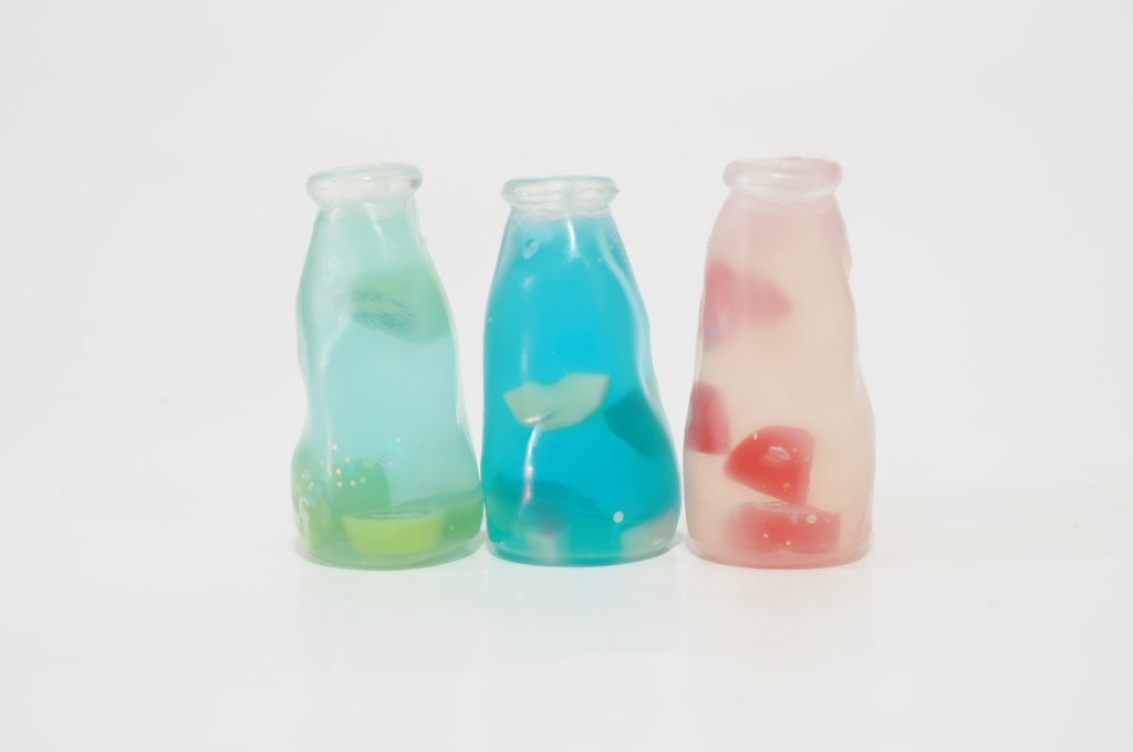 Three fruit drink bottle-shaped oil squishy toys in apple, kiwi, and watermelon varieties, displayed together with colorful fruit-themed designs.