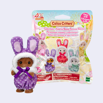 Brown Calico Critters baby figure wearing a purple polka-dot bunny costume with long ears and a purple bow, standing beside a Colorful Bunny Costume Babies blind bag.