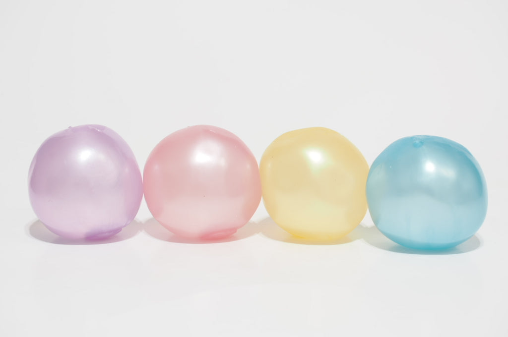 Four translucent oil-filled squishy balls in purple, pink, yellow, and light blue, arranged side by side on a white background.
