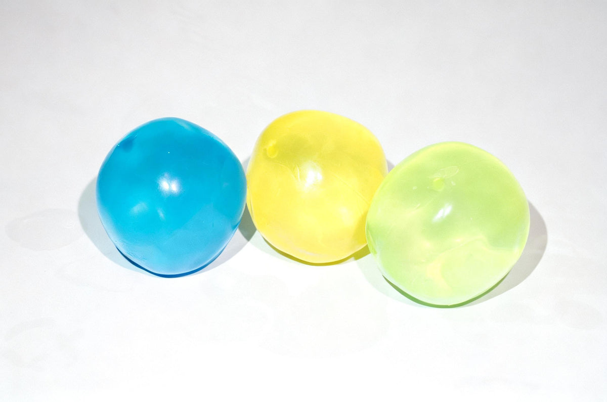 Three translucent Oil Squish balls in blue, yellow, and light green, arranged in a row on a white background.