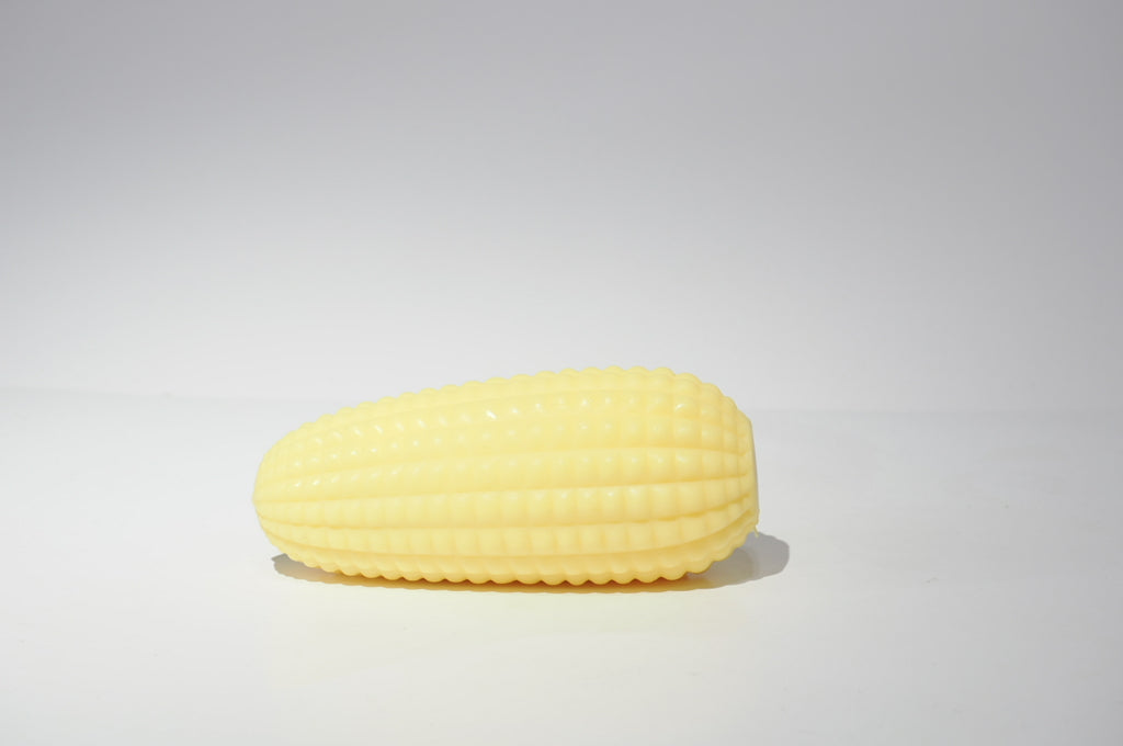 Yellow crunchy corn squishy toy lying horizontally on a white surface, showing its elongated shape and rounded ends.