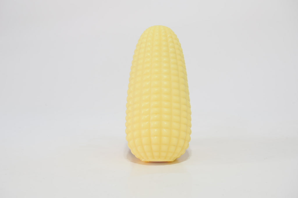 Yellow corn-shaped crunchy squishy toy standing upright on a white surface, showing its long, rounded shape and textured corn-like exterior.