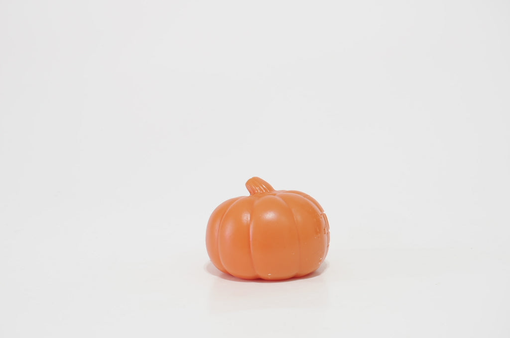 Rear view of an orange pumpkin-shaped crunchy squishy with smooth rounded ridges and a short stem on top, standing against a white background.