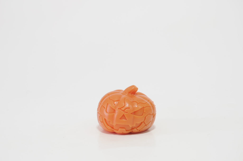 Orange pumpkin-shaped crunchy squishy with an angry jack-o'-lantern face, triangular nose, jagged grin, molded pumpkin ridges, and a short stem on top, against a white background.