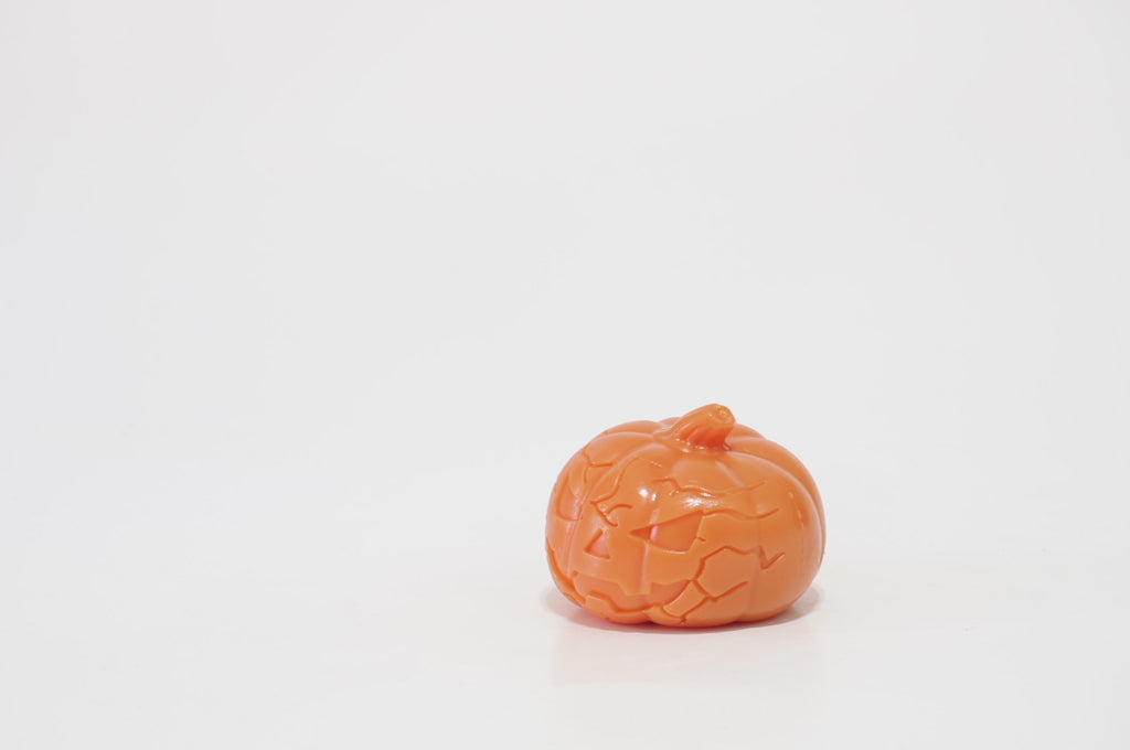 Side-angle view of an orange pumpkin crunchy squishy, showing its rounded shape, molded grooves, short stem, and partially visible jack-o'-lantern face.