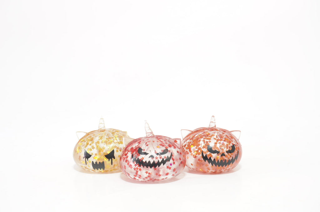 Three Halloween Mystery Spooky Triplets Dumplings squishy toy designs in yellow, pink-red, and orange, featuring black jack-o'-lantern-style faces and colorful star patterns, displayed against a white background.