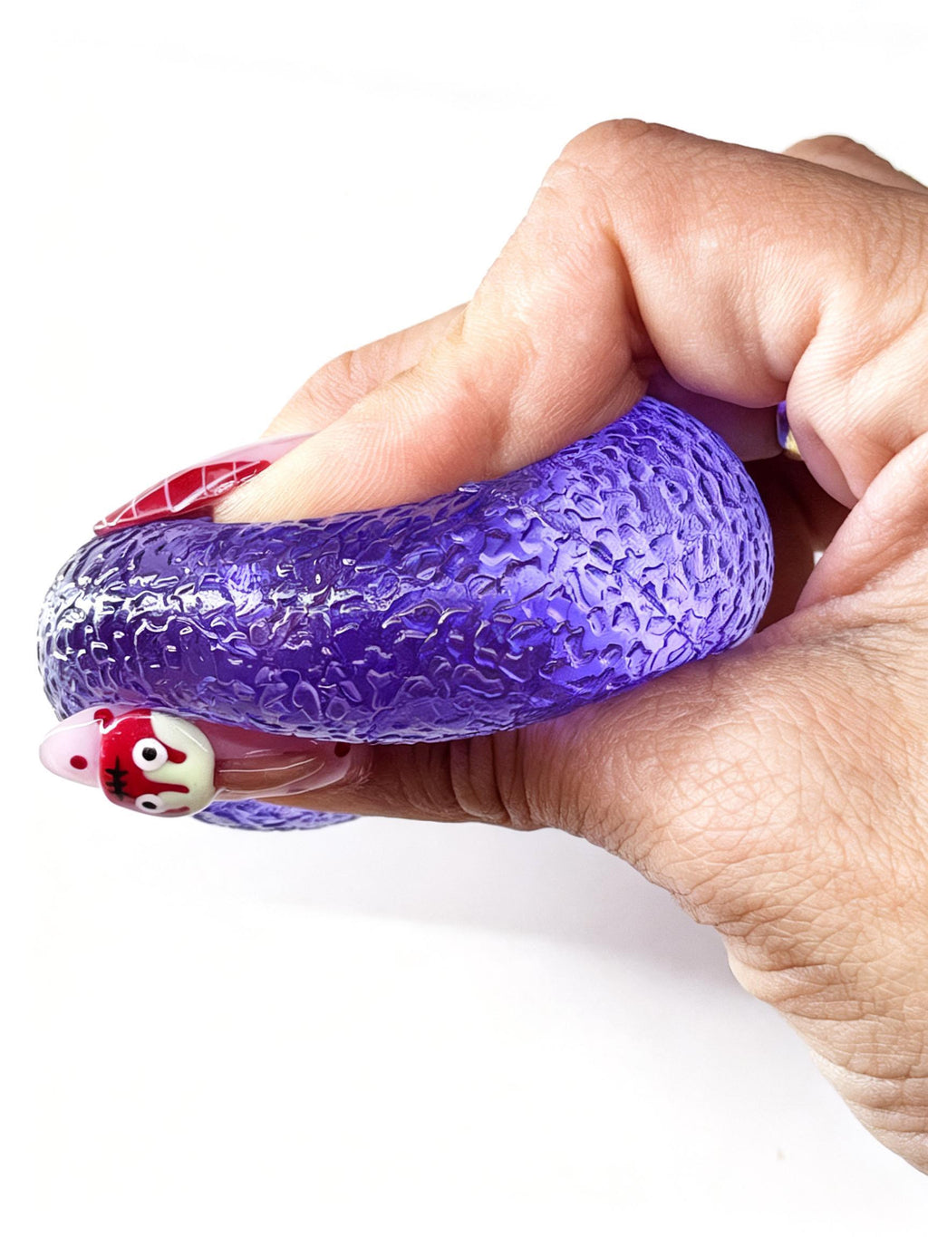 A hand compresses the purple gumdrop squishy into a flattened shape across the palm.