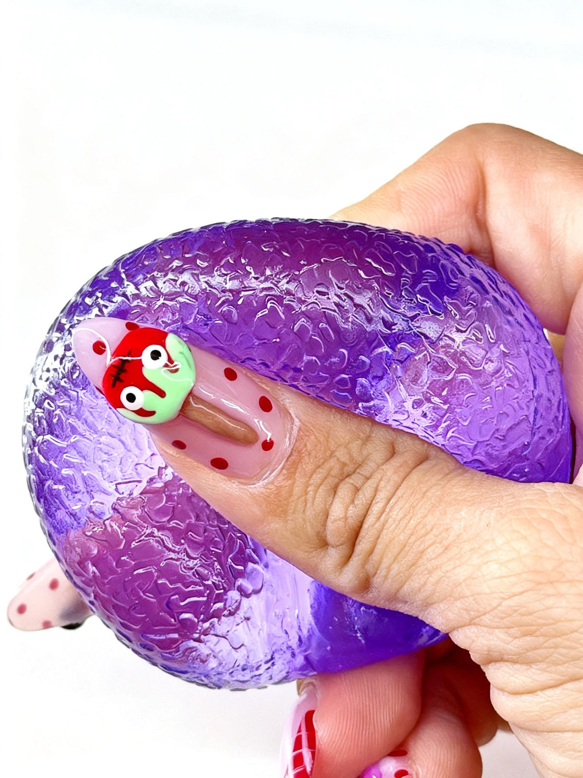 A thumb presses deeply into a purple gumdrop squishy, forming a curved indentation.